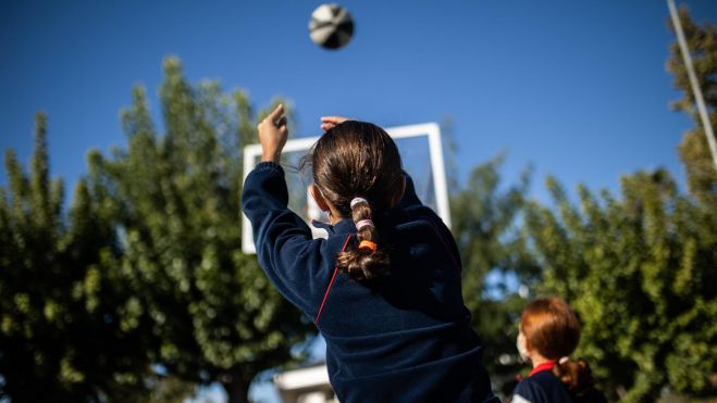 Una xiqueta juga al bàsquet al pati d'un col·legi