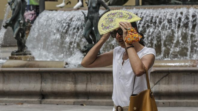 Mujer protegiéndose del sol con un abanico en la plaza de la Virgen durante una ola de calor