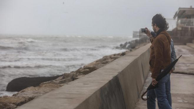Dos personas fotografían el mar, en la Playa de la Malvarrosa, durante un temporal de viento. Imagen de Rober Solsona