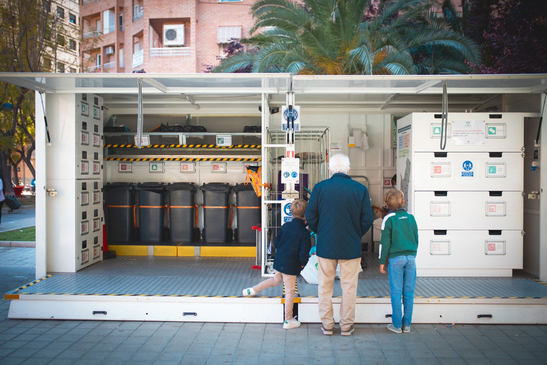 Dos niños y su abuelo observan un ecoparque móvil. Imagen: EMTRE