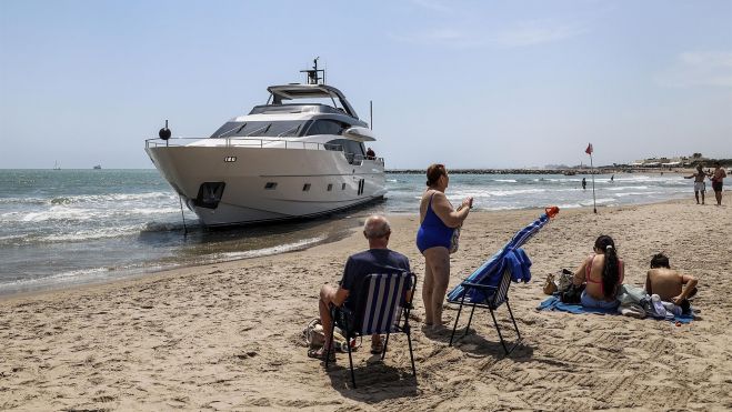Un grupo de bañistas sentados frente al yate encallado en la playa de Pinedo Un grupo de bañistas sentados frente al yate encallado en la playa de Pinedo
