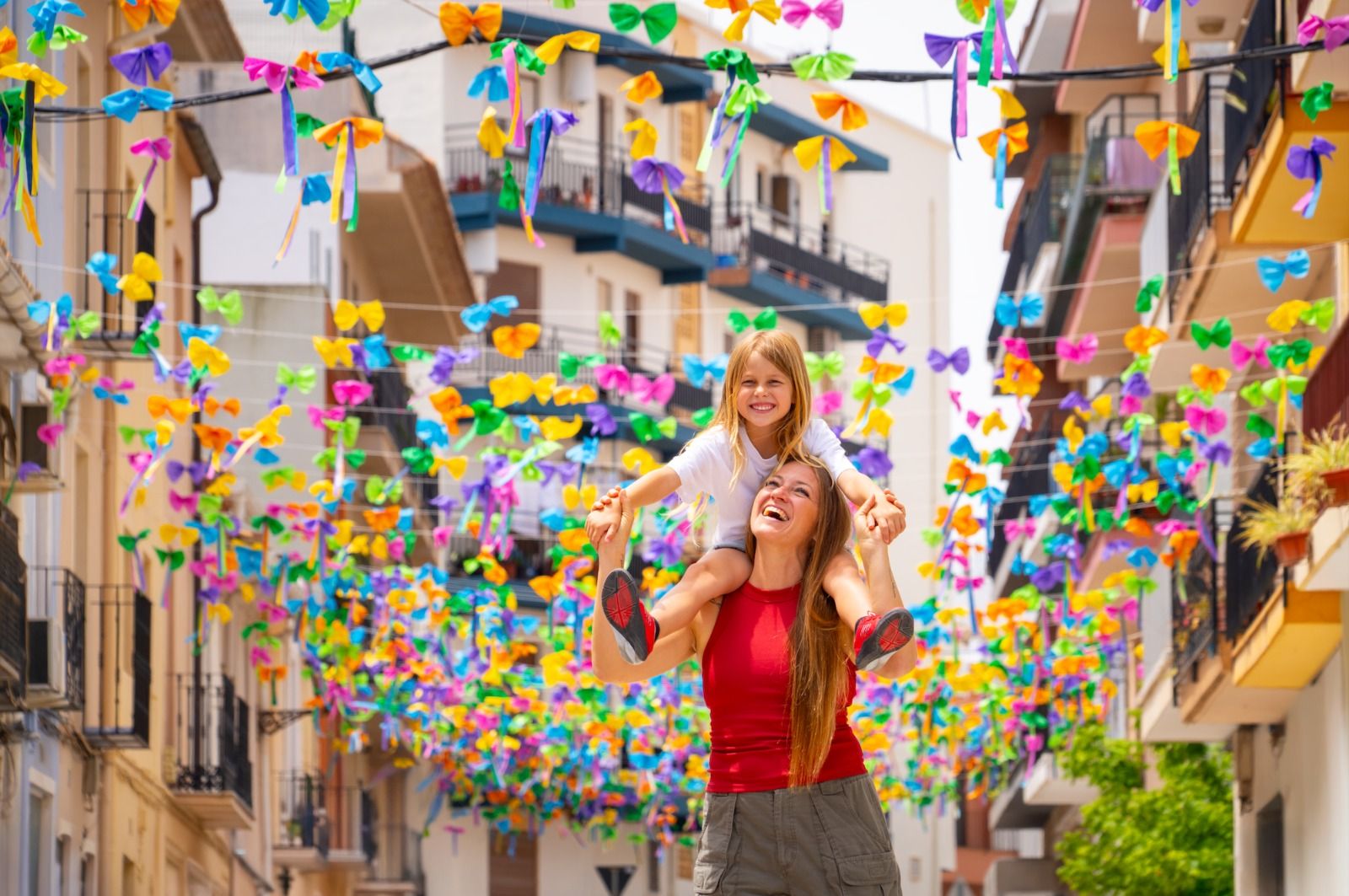 Una mare i la seua filla passegen per un centre històric de Benissa replet de banderoles de colors
